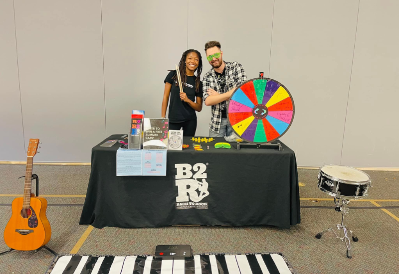 male and female bach to rock employee at an event table with a prize wheel and musical instruments